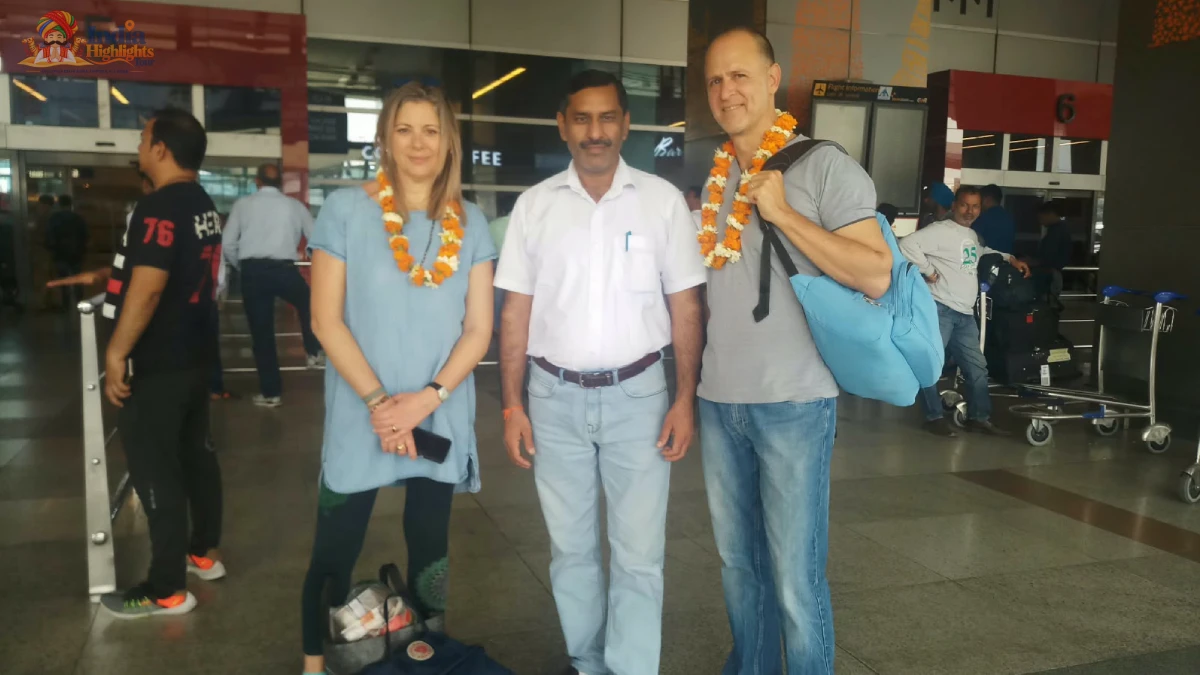 Travelers in casual wear adorned with floral garlands posing with India Highlights representative at the airport