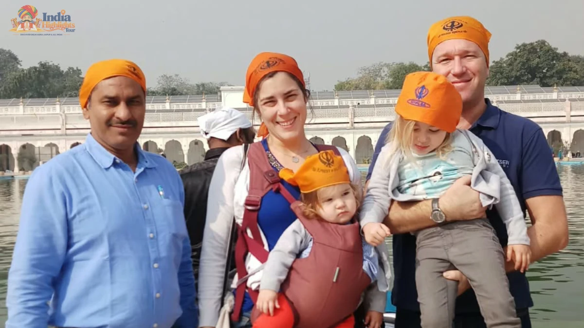 Foreign family with toddlers wearing saffron head scarves posing beside the sacred sarovar at Gurudwara Bangla Sahib in Delhi