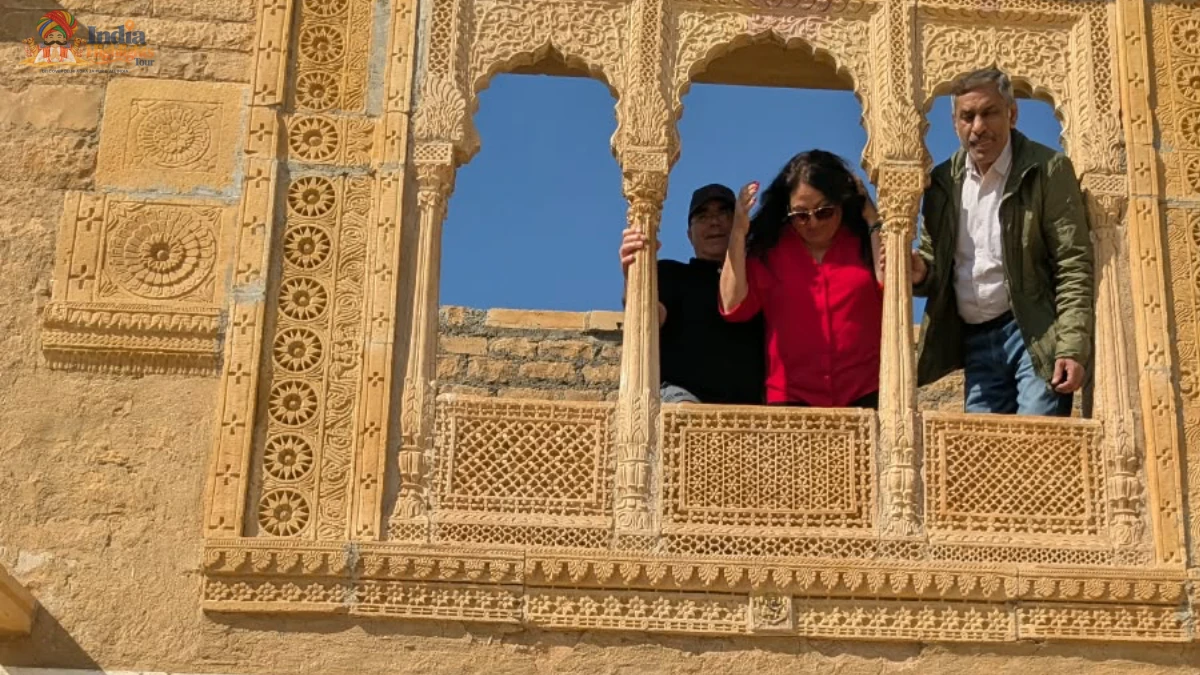 Tourists and guide looking out from an intricately carved yellow sandstone jharokha balcony in Jaisalmer Rajasthan