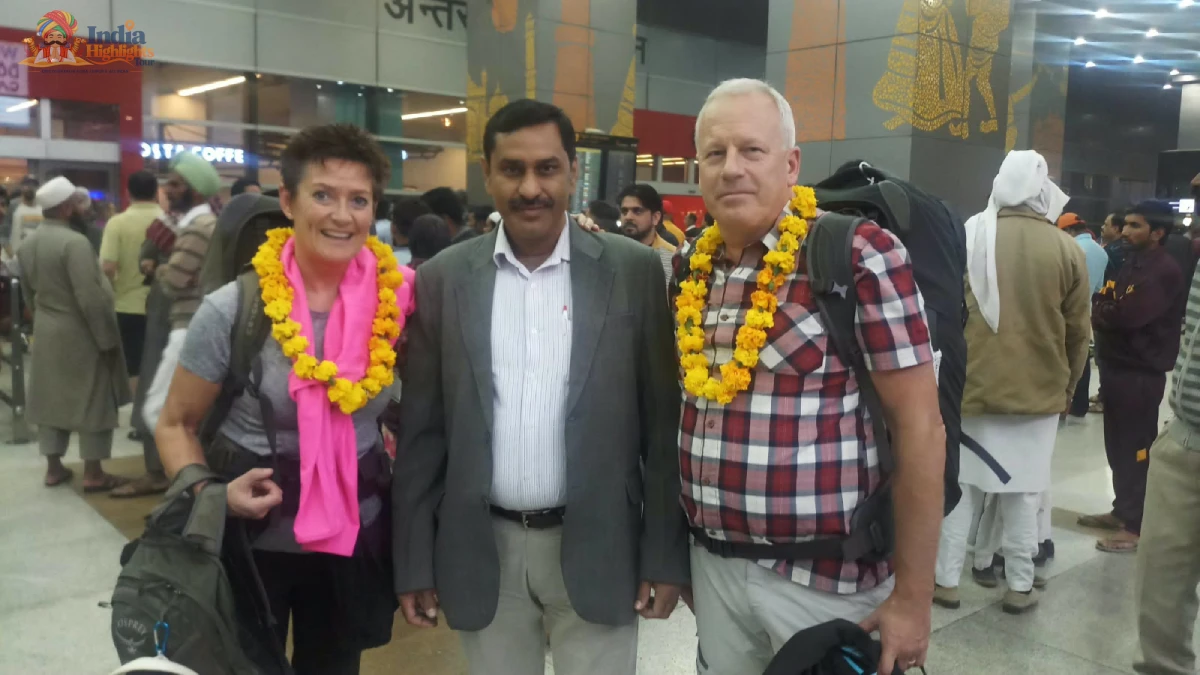 International travelers with backpacks wearing traditional marigold garlands alongside tour manager at Delhi Airport